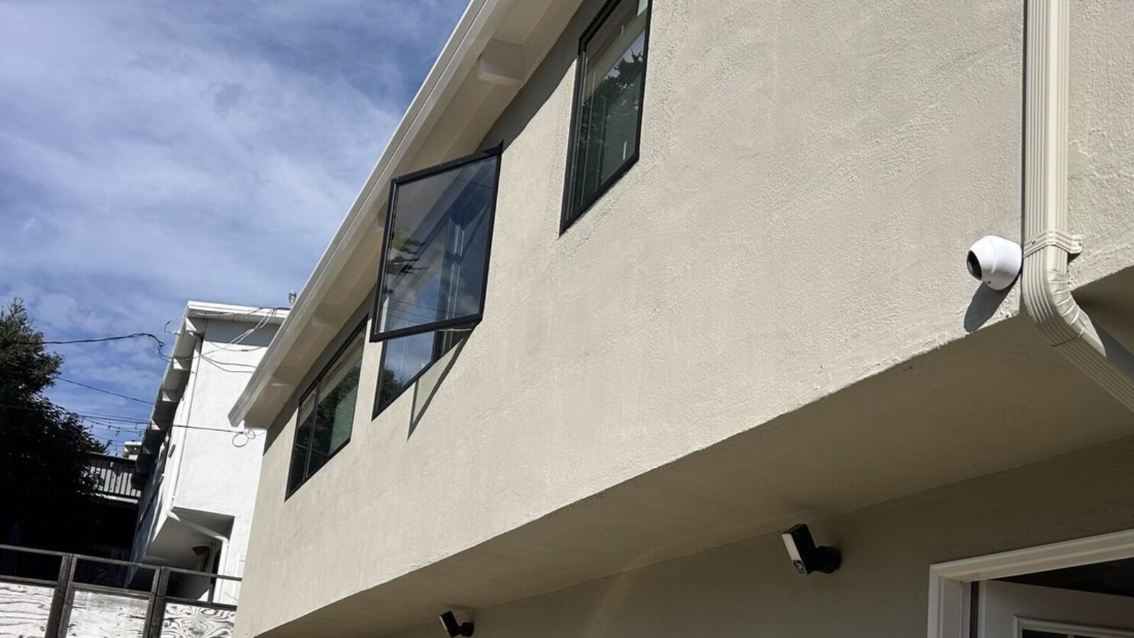 Real exterior security camera mounting context showing wall surface, eave height, downspout clearance and entry-side camera placement
