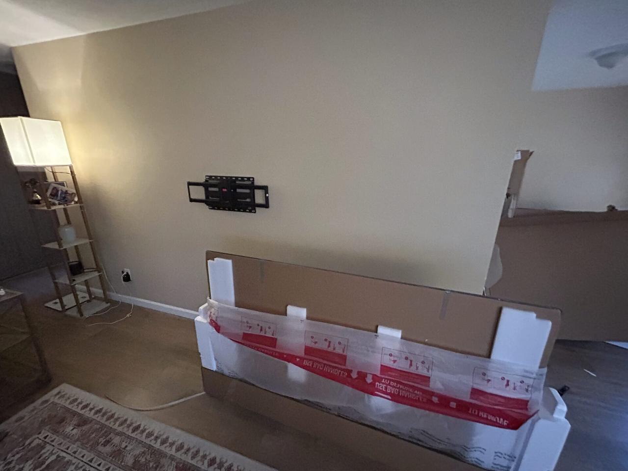 TV mounting preparation with bracket placement and large boxed screen below the wall